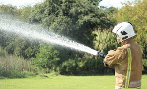 A firefighter spraying water on a field Description automatically generated